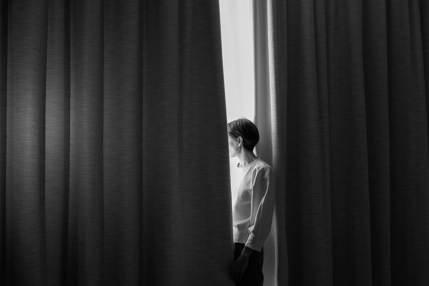 A woman parts heavy curtains toward the light