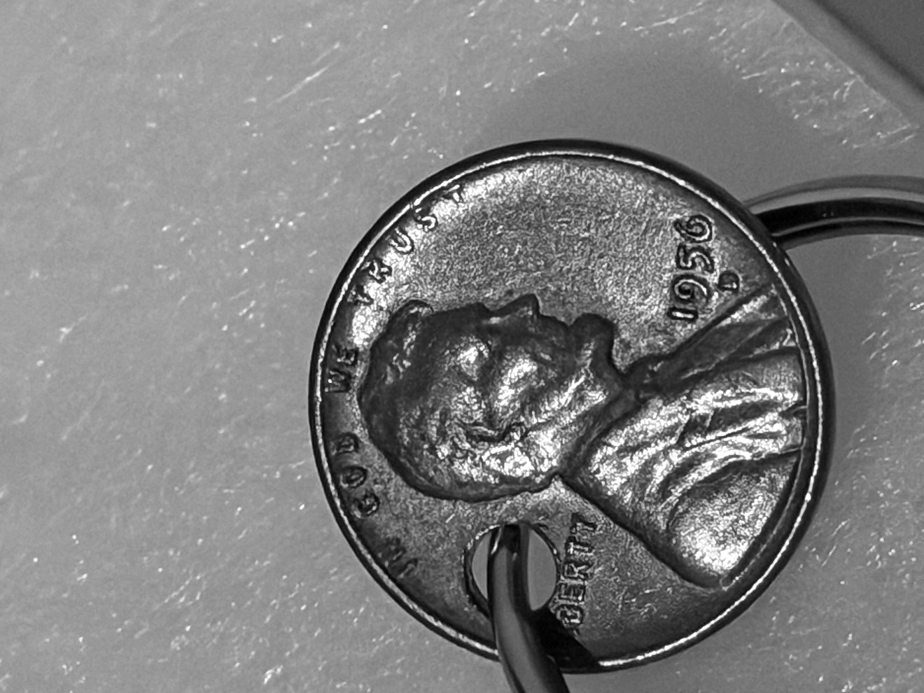 A worn 1956 Lincoln penny on a key ring, drilled through just above Lincoln's ear, lying on a pale countertop.