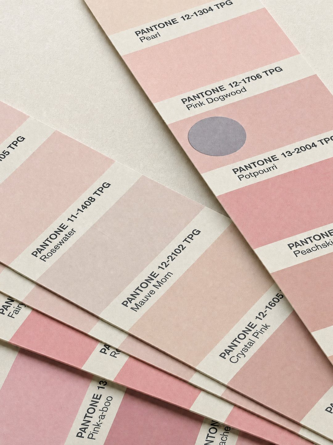 Pantone colour specifier pages fanned across a pale ground, showing a range of pinks including Pearl, Pink Dogwood, Rosewater, Mauve Mom, Crystal Pink and Pink-a-boo.